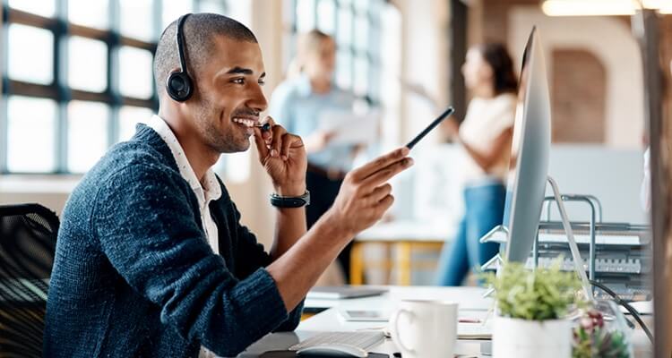 Smiling man with headset points to monitor with pen