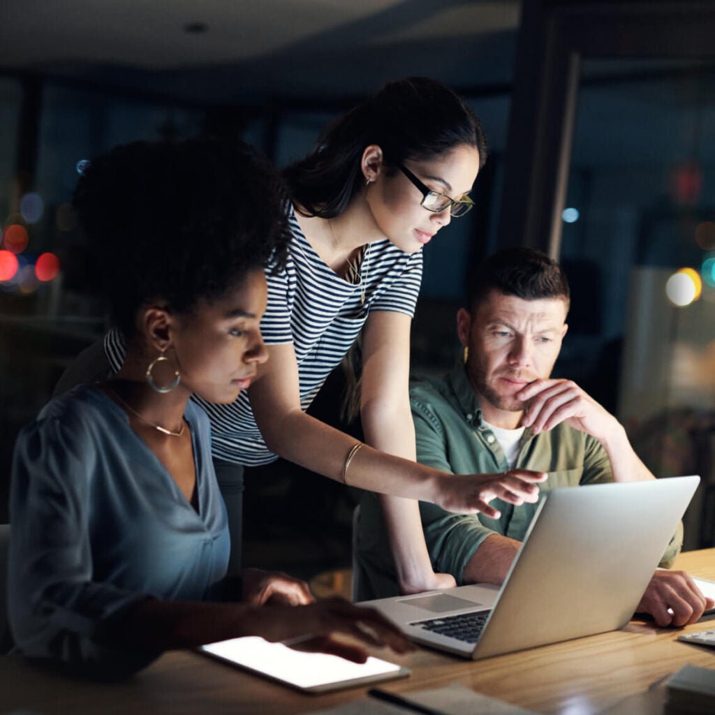 Three people working on a laptop at a desk.