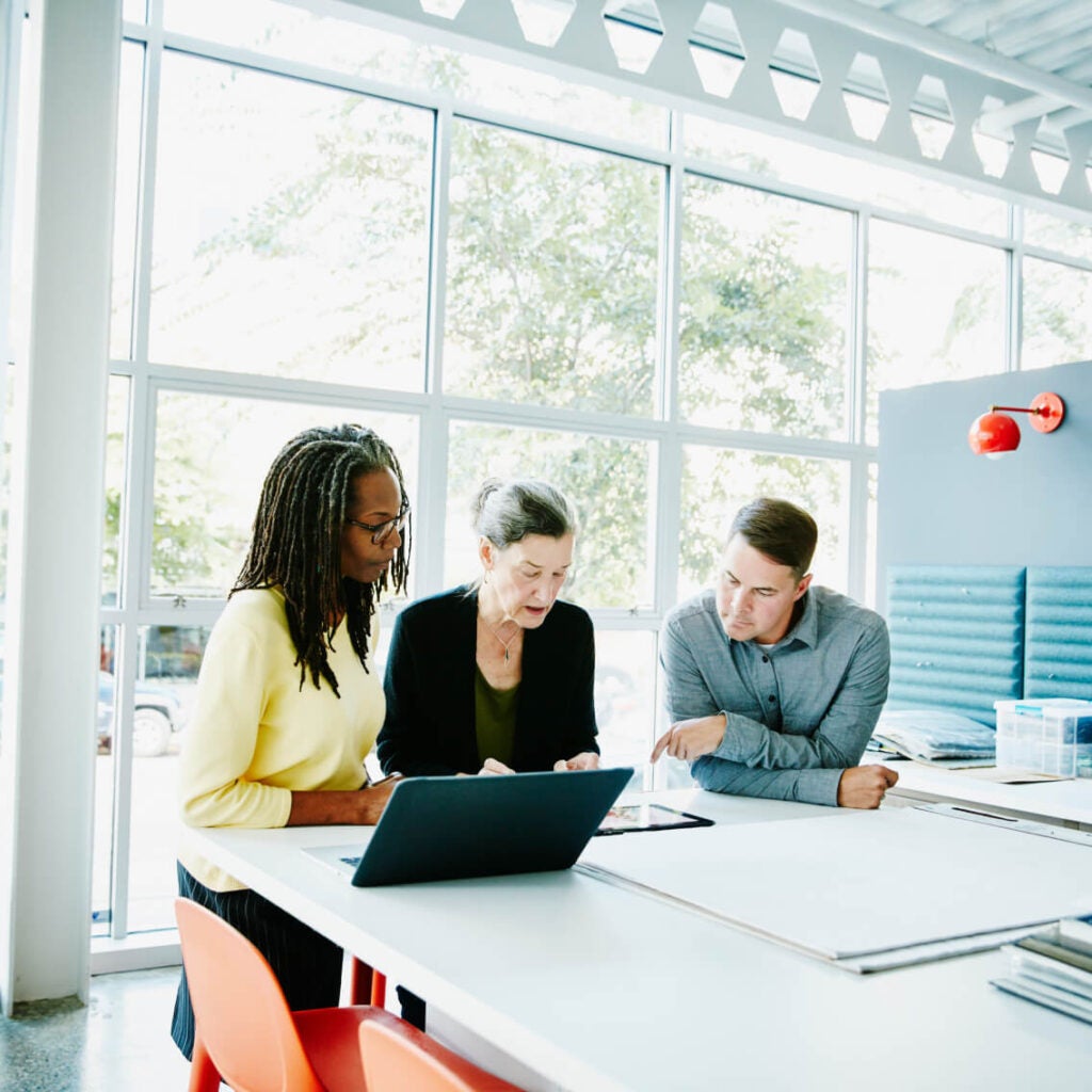 Three people working off a laptop at a table.