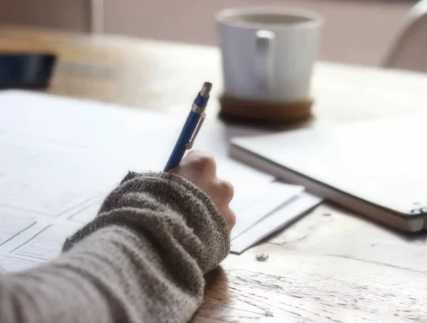 Person taking notes with a pen and paper at a desk.