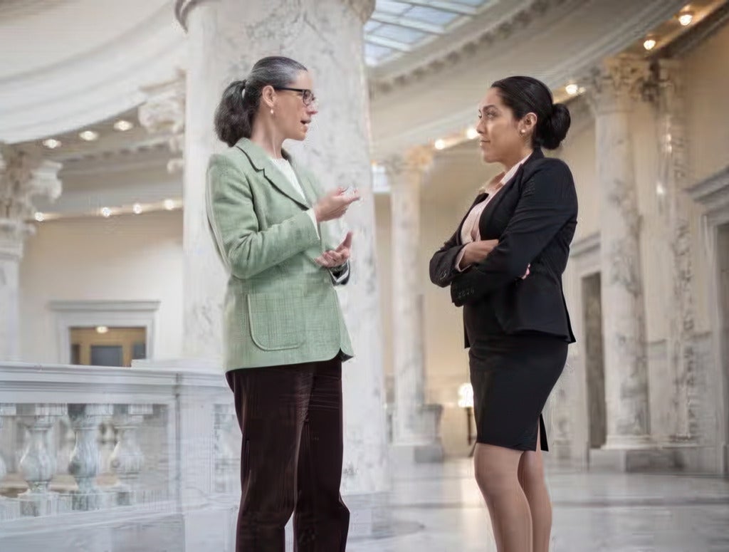 Two business women having a conversation in the hallway of a government building.